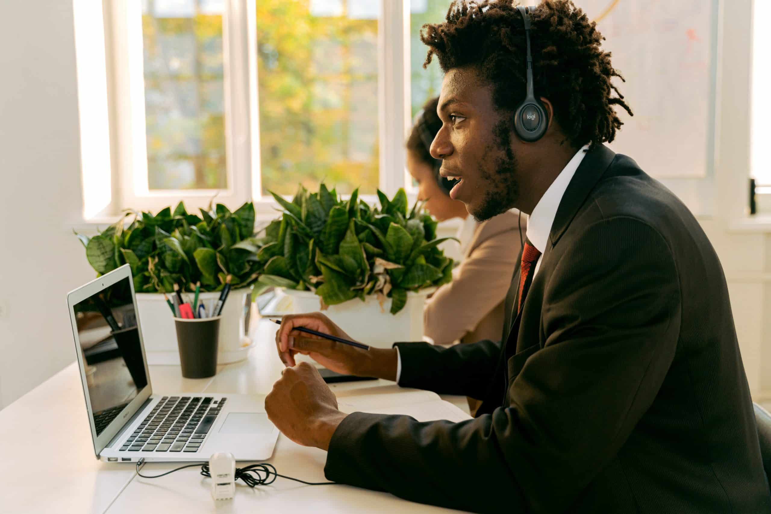 A picture of a professional wearing a suit and sitting in front of a laptop while speaking into headset to represent the managed service provider industry that offers IT solutions to SMBs up to enterprise organization networks.