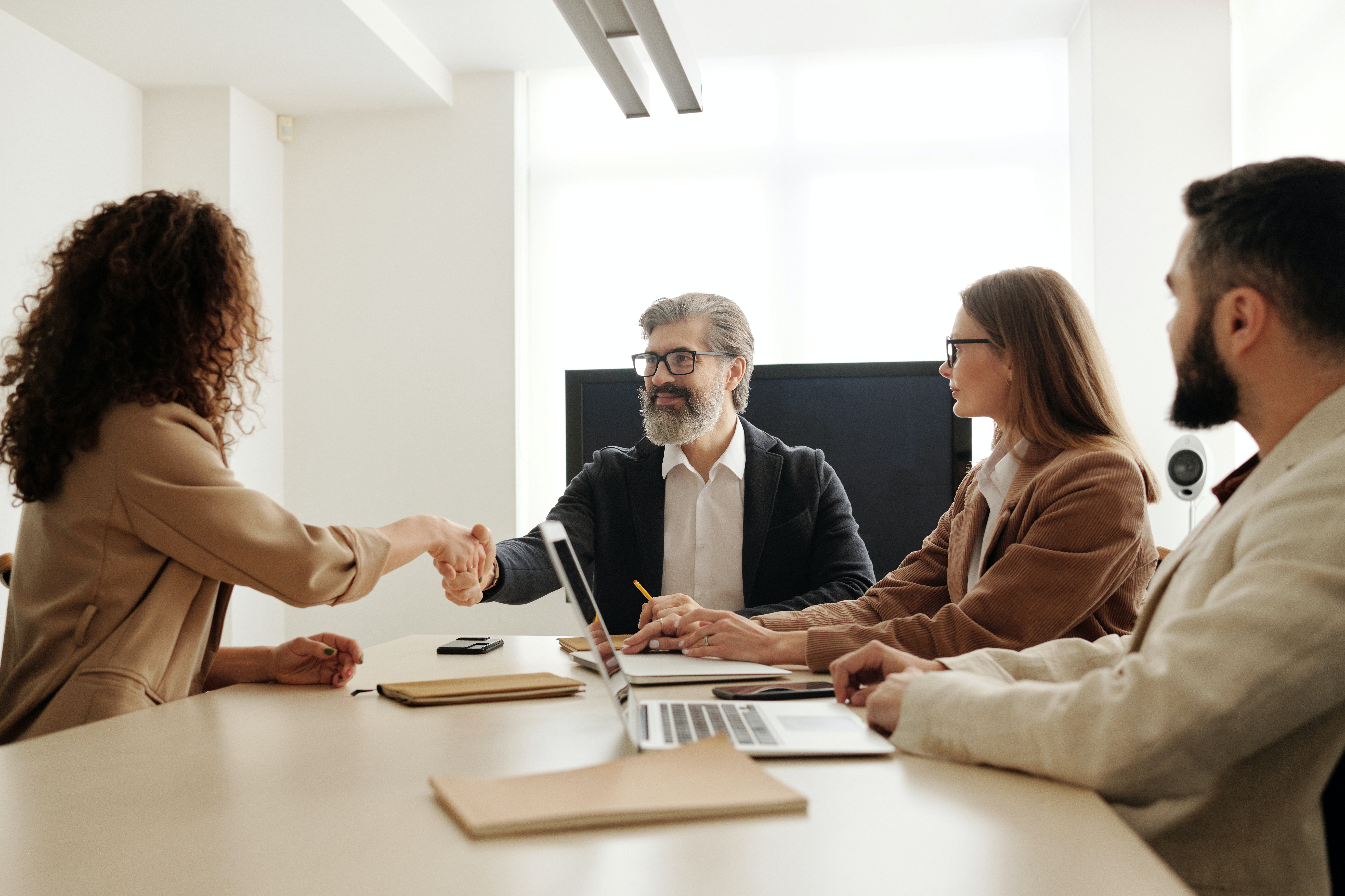A picture of two professionals shaking hands at a conference table as this article is about Partner Relationship Management aka PRM software, where vendors can optimize their channel partner programs by automating common industry process for sales, marketing, and enablement.