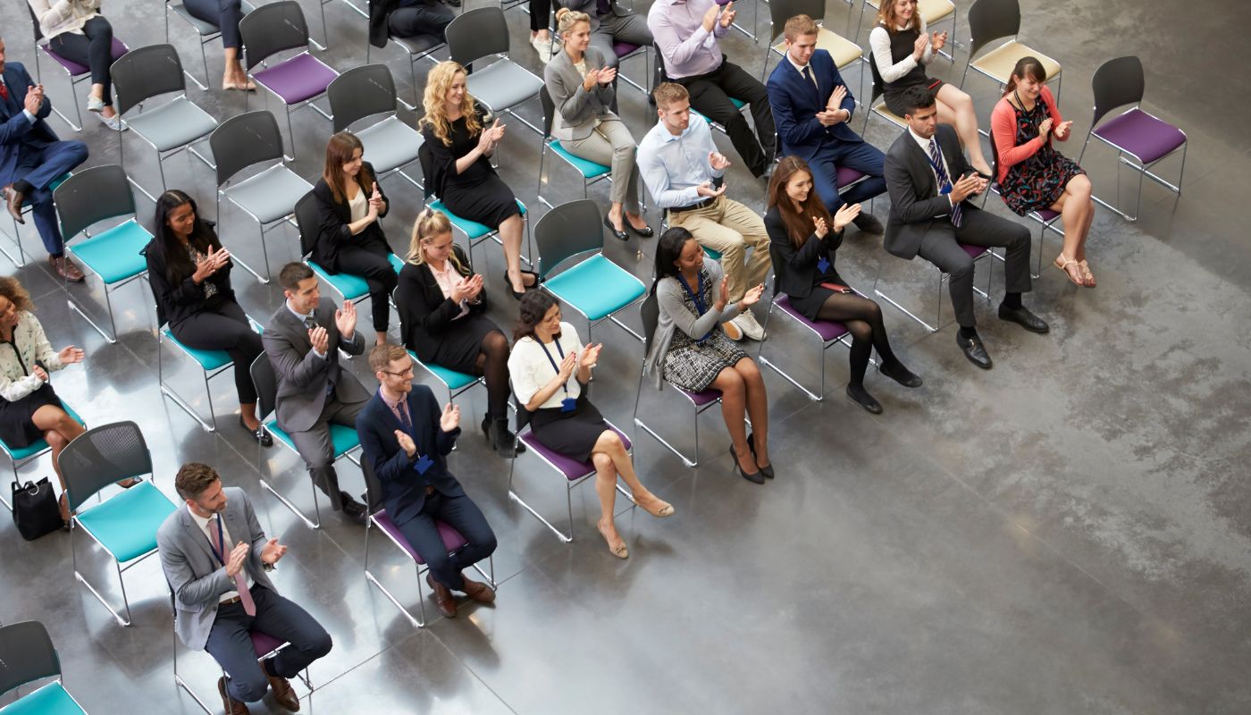 Overhead View Of Audience Applauding Speaker At Conference.